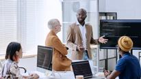 African businessman standing near the screen with presentation and presenting new software to programmers at meeting