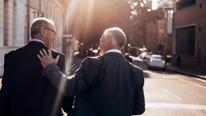 Vue arrière de deux hommes d’affaires marchant en bavardant à l’extérieur d’un immeuble de bureaux après une réunion d’affaires réussie.Professionnels de haut niveau marchant ensemble par une journée ensoleillée.