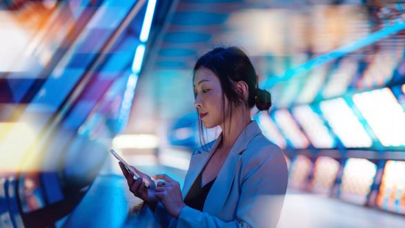 Young business woman holding smartphone with a computer generated background. Innovation, metaverse and futuristic concepts.