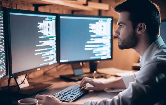 Man Looking at Code on Two Monitors