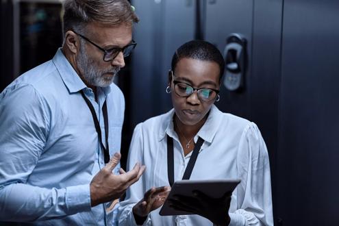 IT technicians using a digital tablet in a server room. Programmers fixing a computer system and network while doing maintenance in a datacenter. Engineers updating security software on a machine