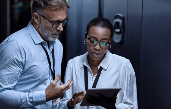 IT technicians using a digital tablet in a server room. Programmers fixing a computer system and network while doing maintenance in a datacenter. Engineers updating security software on a machine