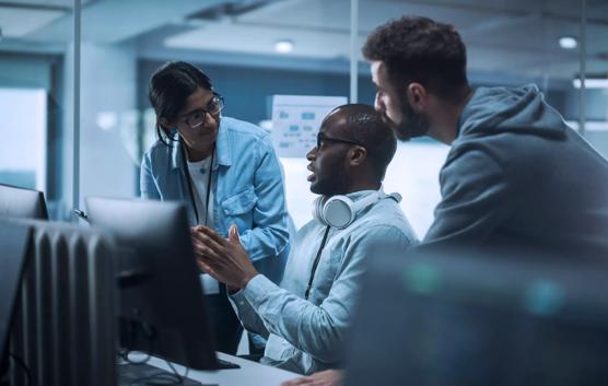 Diverse Group of Professionals Meeting in Modern Office: Energetic and Enthusiastic IT Programmers Use Computer Together, Talk Strategy, Discuss Planning. Software Engineers Develop Inspirational App