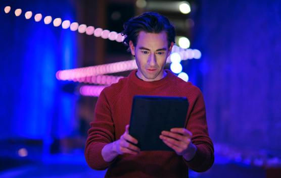 A young man using a digital tablet at night in a city with blurred lights.