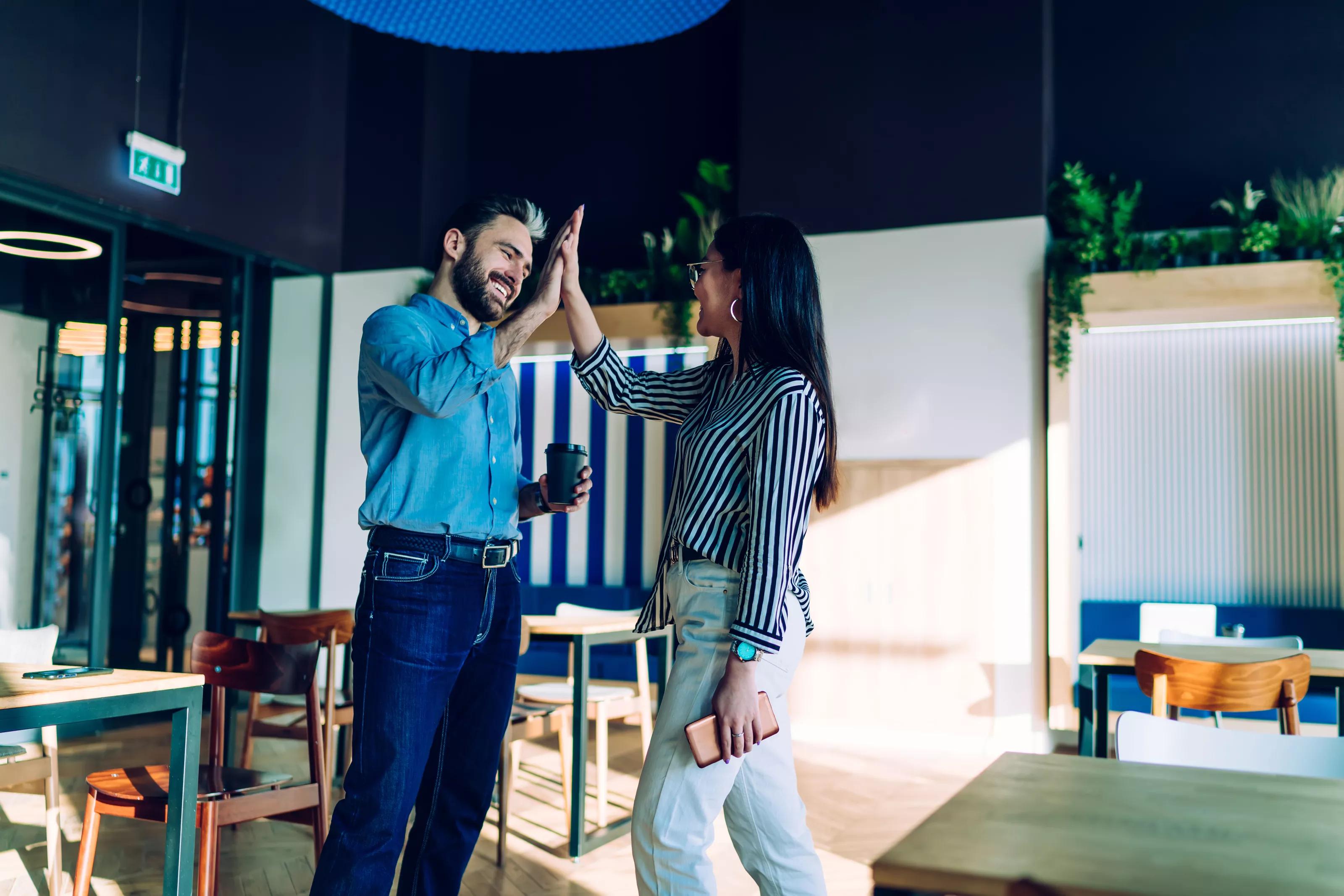 Smiling adult male manager in casual formal wear praising female coworker and giving high five at modern stylish work space