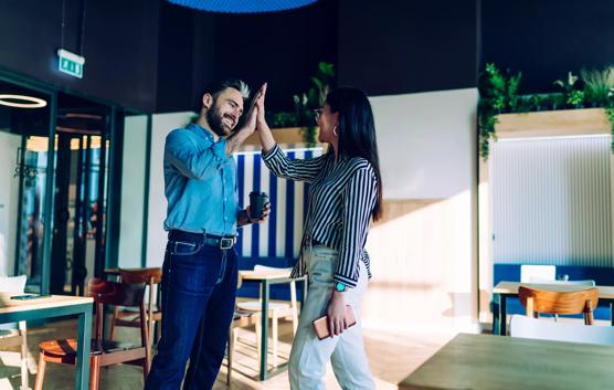 Smiling adult male manager in casual formal wear praising female coworker and giving high five at modern stylish work space