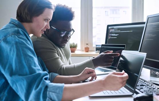 Female programmer pointing at laptop with software and consulting with colleague about computer codes