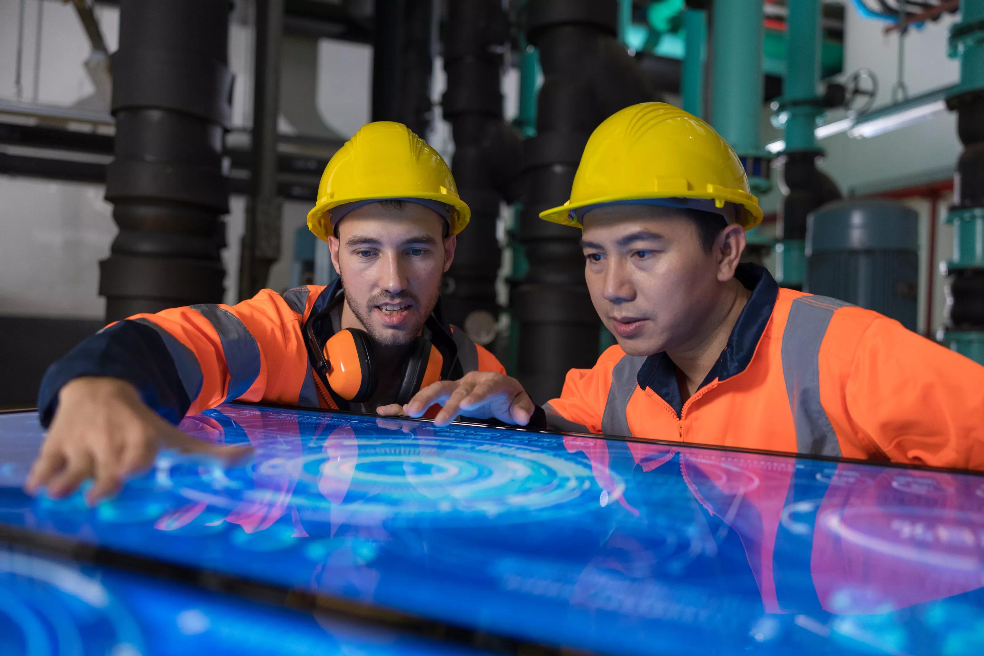 Two male engineer working at Illuminated table display with futuristic smart function for finding solution in the machine room.