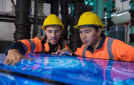 Two male engineer working at Illuminated table display with futuristic smart function for finding solution in the machine room.