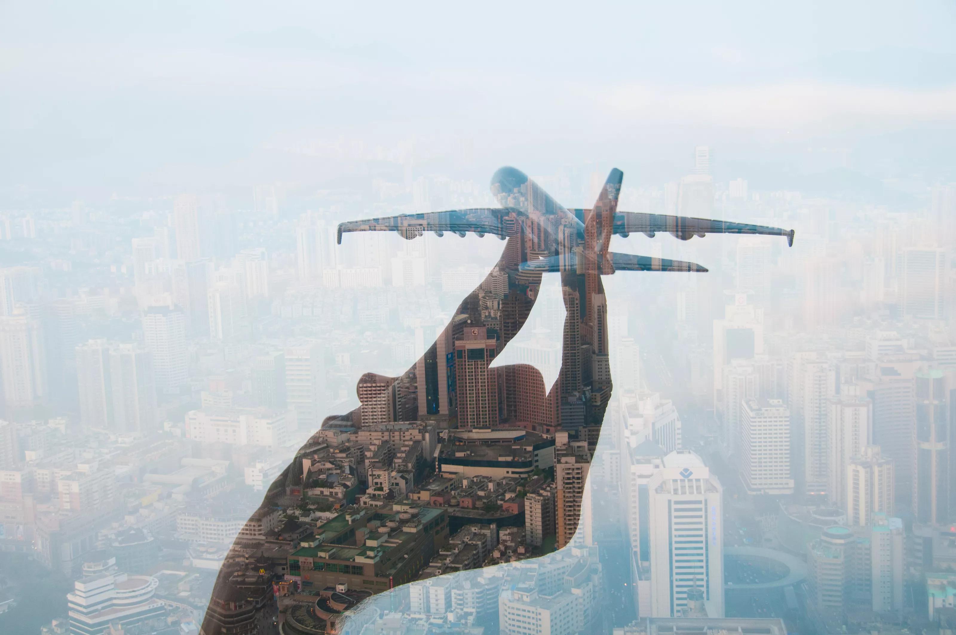 double exposure of mans hand holding a toy plane and cityscape in the background