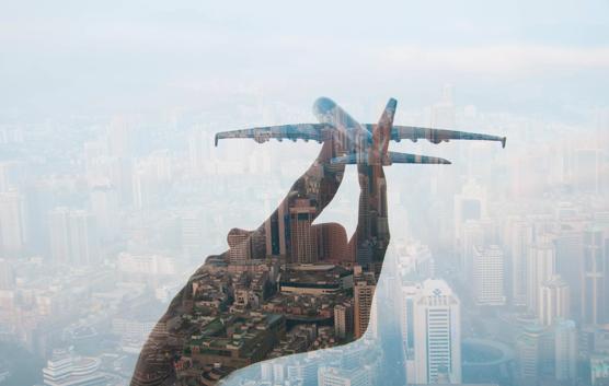 double exposure of mans hand holding a toy plane and cityscape in the background